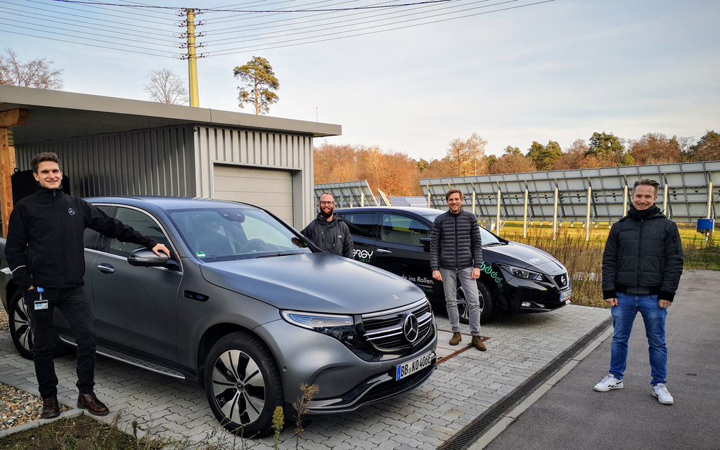 Elektroautos vor Elektrotankstelle und Forscherteam. Für die Mobilitätswende kann der Energieverbrauch mit der App eingetragen und berechnet werden. Technologie für die Energiewende, bei der man die Tageskilometer mit dem Elektrofahrzeug 